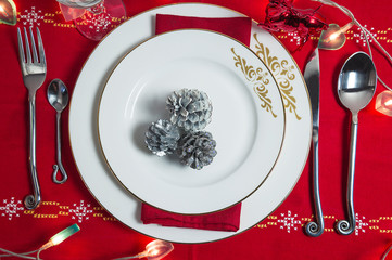 Wall Mural - Festive table setting for christmas or new year dinner. White plates, cutlery, wineglasses, red napkin and christmas decorations on the red tablecloth. Top view, close up