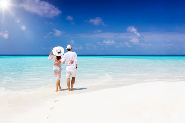 Wall Mural - A hugging honeymoon couple walks down a tropical beach with turquoise sea and sunshine 