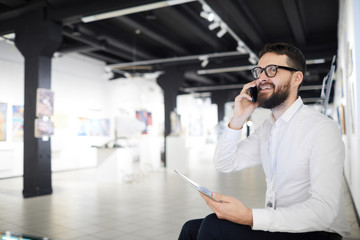 Portrait of bearded art gallery manager speaking by phone while preparing for exhibition in museum, copy space