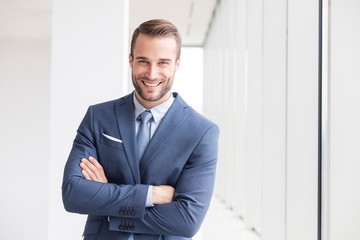 Portrait of smiling handsome young businessman standing with arms crossed in new office