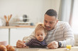 © Seventyfour - Warm-toned portrait of caring father with cute little girl using digital tablet together while sitting at wooden table in cozy kitchen, copy space
