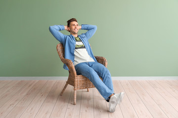 Poster - Handsome man sitting in armchair near color wall