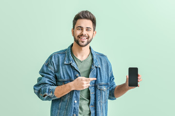 Wall Mural - Happy young man with mobile phone on color background