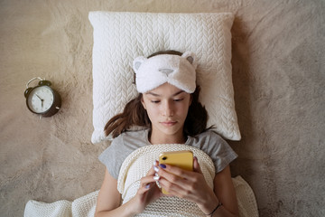 Wall Mural - Cute teen girl woke up in the morning at home and using smartphone   