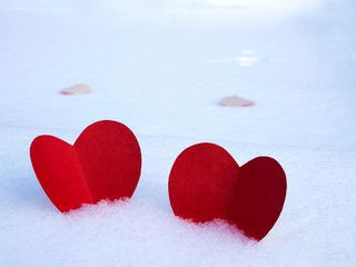 Red paper hearts on white snow as a symbol of love and warmth.