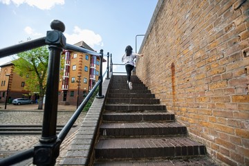 Wall Mural - Full length rear view of young woman walking up stairs outdoors