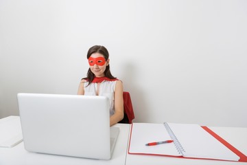 Young businesswoman dressed as superhero using laptop at desk in office