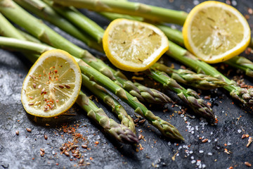 Fresh asparagus dish with lemon and spices on black plate closeup.