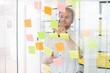 © MDBPIXS - Young businessman reading sticky paper on glass wall at creative office