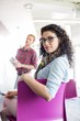 © MDBPIXS - Portrait of confident businesswoman sitting on chair with colleague standing in background at creative office