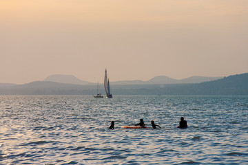 Wall Mural - Lake Balaton at sunset in back light with sailboats and silhouettes of bathers.