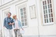 © MDBPIXS - Happy middle-aged tourist couple walking arm in arm by building