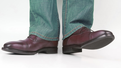 Male legs in jeans and brown classic shoes on white background