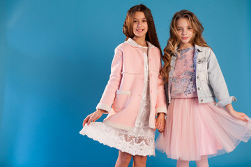 Portrait of two beautiful fashionable girls in a white dress and pink winter jacket