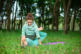 Fototapeta Dmuchawce - A young sports girl practices yoga in a quit green summer forest, yoga assans posture. Meditation and unity with nature