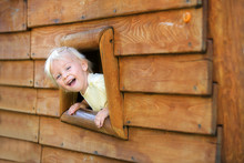 Curious Child, Toddler Boy, Peering From A Small Window In Wooden Shrub