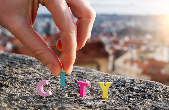 word City of colored letters on the background of the city. fingers put one letter in a word