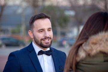 Young attractive man with a beard dressed in suit and bow tie talking to a young woman