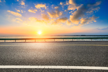 Empty asphalt road and lake with dreamy clouds at sunset.