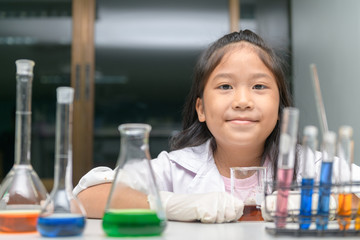 Wall Mural - happy little girl wearing lab coat making experiment.