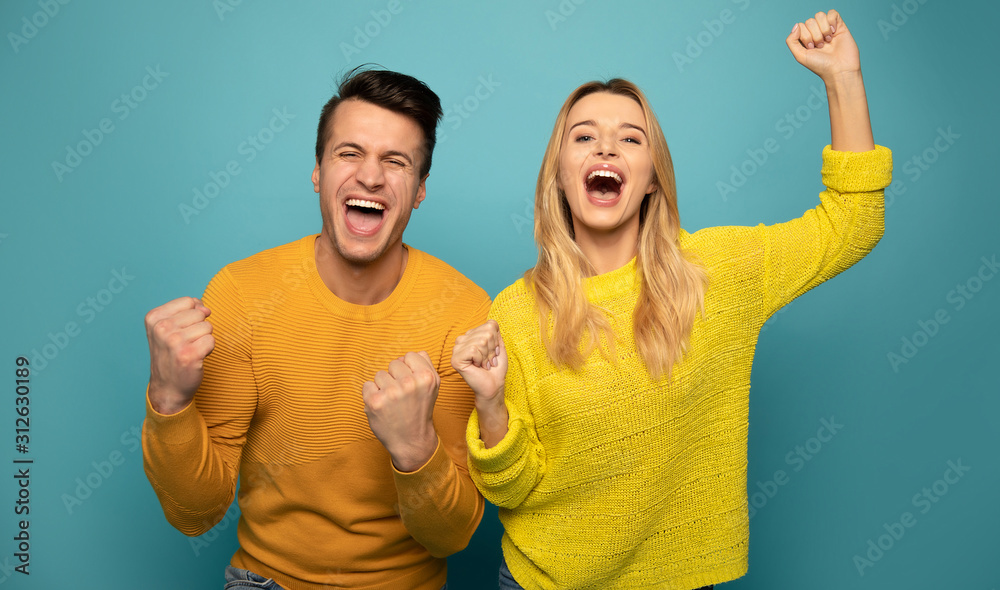 Joyful mood. Excited couple is posing on emerald background, wearing yellow sweaters and expressing happiness and victory with their poses, gestures and facial expressions. - obrazy, fototapety, plakaty 