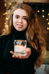 Wall Mural - Girl dressed in black clothes holding a glass with a candle in the hands.