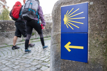 Wall Mural - Way of St. James sign and unfocused pilgrims at background. Yellow scallop sign pilgrimage to Santiago de Compostela