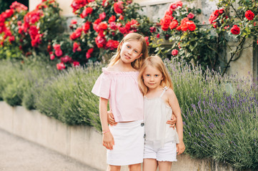 Outdoor portrait of two sweet little girls, kids playing together, fashion for young children