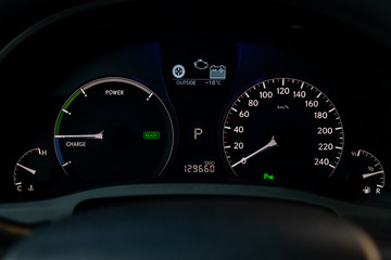 Wall Mural - The dashboard of  car is glowing white with arrows at night with a speedometer, charge battery level and other tools to monitor the condition of the hybrid vehicle in modern style on black background