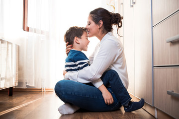 mom and her son hugging each other. mom is kissing her kid in the forehead.