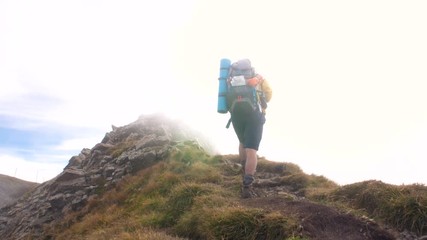 Wall Mural - young man hiker on mountain with cloudy sky and fog. yellow jacket, backpack and beanie. traveling d