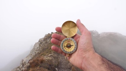 Wall Mural - man hiker hands with compass on mountain with cloudy sky and fog. yellow jacket. traveling dolomites