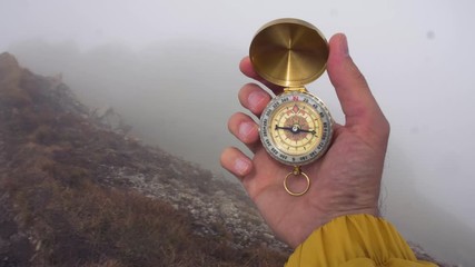 Wall Mural - man hiker hands with compass on mountain with cloudy sky and fog. yellow jacket. traveling dolomites