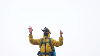 Wall Mural - vr virtual reality headset. young man hiker moving hands on cloudy sky and fog background. yellow ho