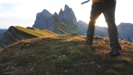 Wall Mural - young man hiking at seceda mountain arriving to peak at sunrise. backpack, yellow jacket, boots, bea