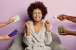 Skin care and beauty concept. Photo of overjoyed Afro American woman in bathrobe clenches fists with happiness, applies facial clay mask on face, rejoices having perfect skin. Hands with cosmetics