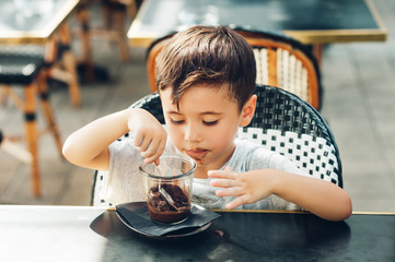 happy little boy eating chocolate ice cream in outdoor cafe