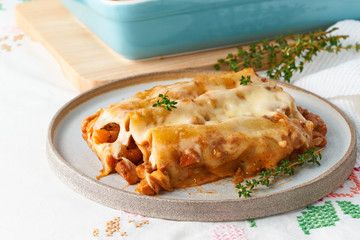 Wall Mural - Cannelloni pasta with filling of ground beef, tomatoes, baked with bechamel tomato sauce and mozzarella. Classical Italian cuisine, white tablecloth with embroidery, rustic style, side view