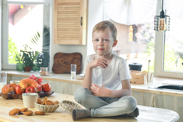 Little caucasian smiling boy sitting on the kitchen table and eat oatmeal cookies with milk. Healthy breakfast before school and kindergarten at home.