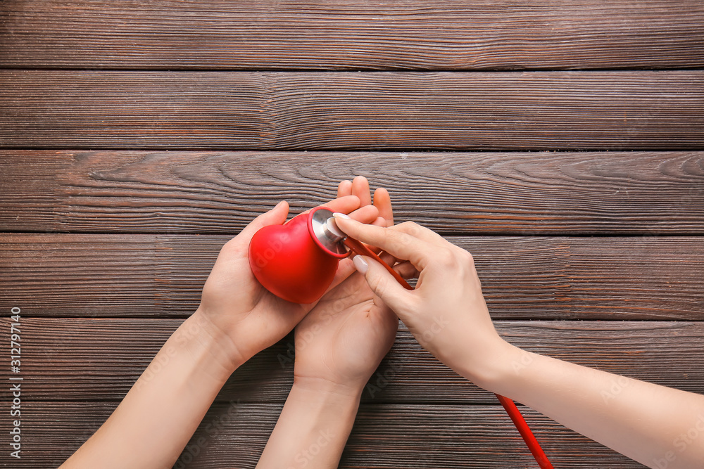 Female hands with heart and stethoscope on wooden background