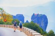 © raisondtre - Hiking young couple tramping on asphalt road in sunset from back. Travel vacation, hiking backpacking, tourism sport and people together concept. Kalambaka, Greece, Monastery Meteora fall view, Europe