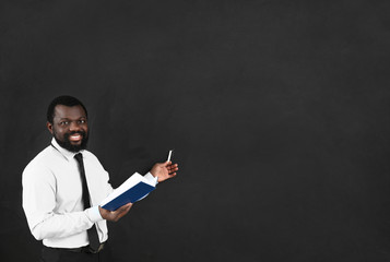 African-American teacher with book near blackboard in classroom