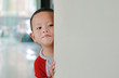 © zilvergolf - Little Asian baby boy hide behind a corner room. Small children playing peekaboo game indoor.