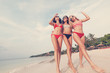 Three beautiful young European slender girlfriends in bright red and striped bikinis walk on a tropical beach on vacation, happiness joy summer and fun