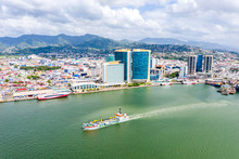 Aerial View Of City Of Port Of Spain, The Capital City Of Trinidad And Tobago. Skyscrapers Of The Downtown And A Busy Sea Port With Commercial Docks And Passenger Catamarans