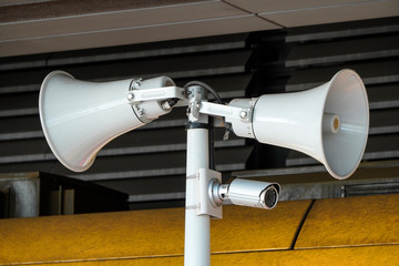 two white loudspeakers and security camera on pole in a public place. providing security in the city