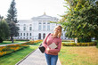 © Марина Демешко - A pretty female student in a polka dot shirt with a beautiful smile is standing on the background of a university and holding a book. Sunny autumn day. Beginning of the academic year