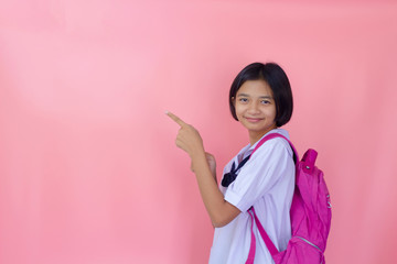 Happy beautiful young Asian girl with backpack in student uniform, pink background.