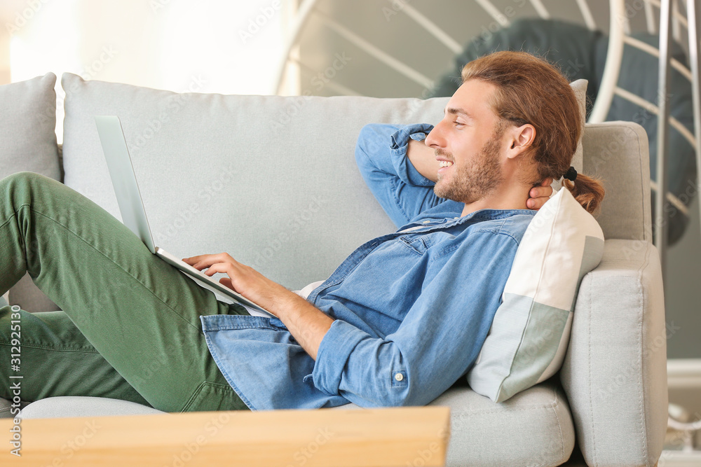 Handsome man with laptop on sofa at home
