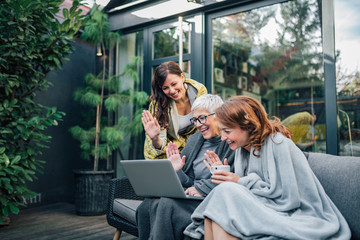 Wall Mural - Family of three beautiful women having video call on laptop in the home garden.